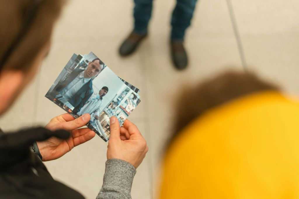 정장 차림의 전경이 된 두 남자의 사진을 들고 있는 손. 배경에 다른 사람의 바닥 타일과 다리가 보입니다.