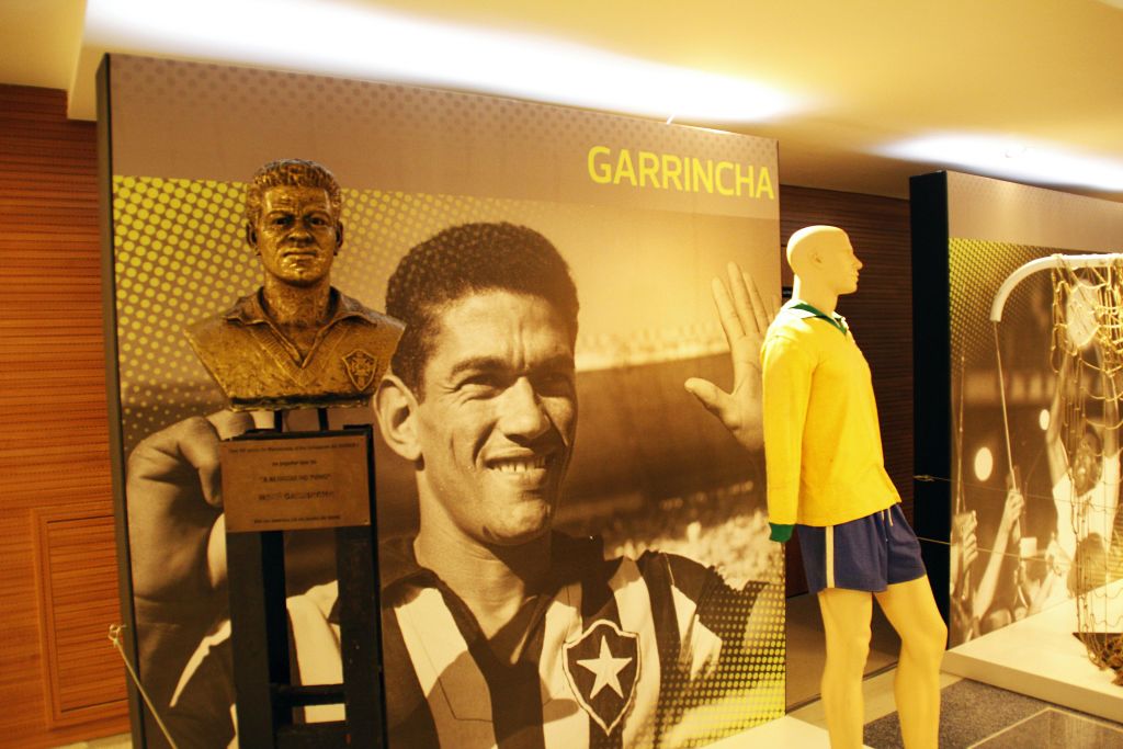 축구 유니폼을 입고 미소를 짓고 있는 커다란 사진 앞에 있는 개린차의 청동 흉상.