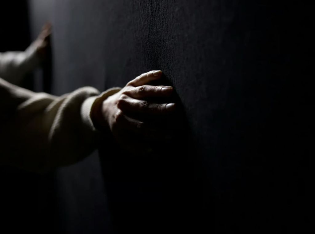 밝은 색 소매의 손이 낮은 조명의 어둡고 질감 있는 벽에 닿습니다.