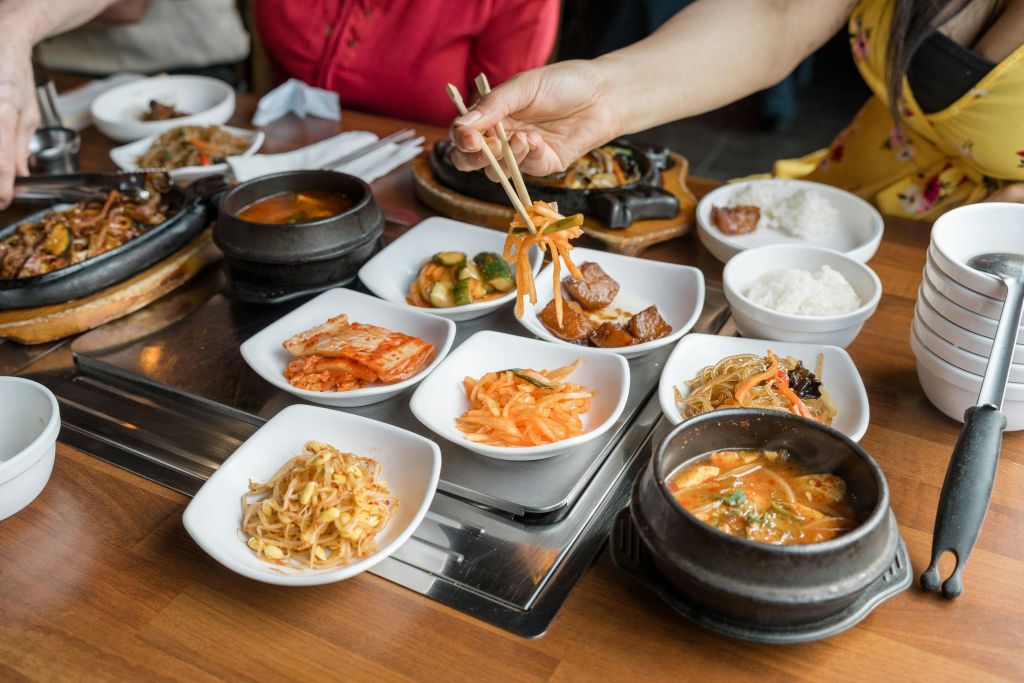 게스트가 젓가락으로 야채를 주워 먹는 한국식 바비큐 반찬이 식탁에 펼쳐집니다.