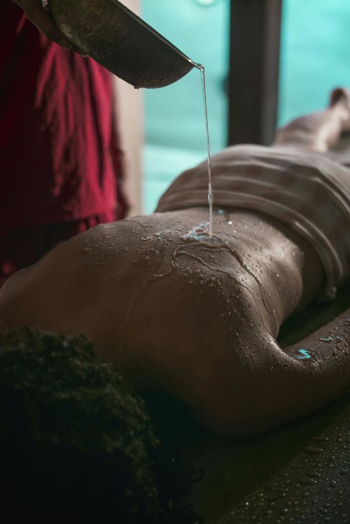 마사지 테이블에 얼굴을 대고 누워 있는 사람의 등에 수건으로 부분적으로 덮인 채 부어지는 물.
