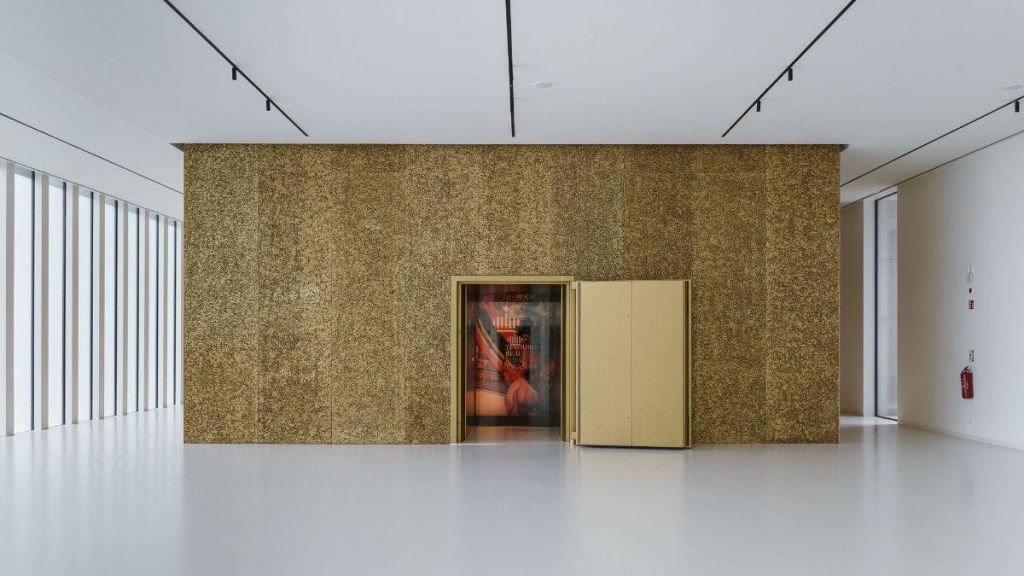 문이 열려 있는 황금색 벽이 있는 미니멀한 객실로, 내부가 흐릿한 형상과 물체가 있는 다채로운 인테리어가 돋보입니다.