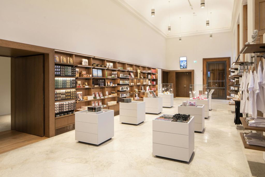 제품들이 늘어서 있는 나무 선반, 여러 개의 흰색 진열대, 위에 있는 펜던트 조명이 있는 현대적인 매장 인테리어입니다.