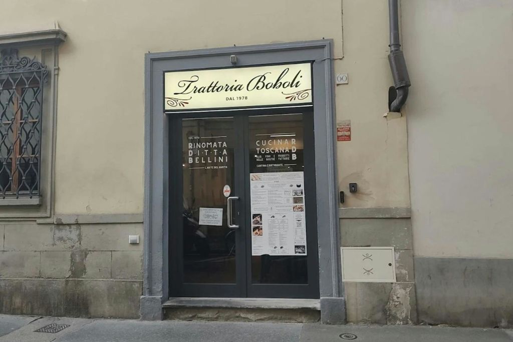 "Trattoria Boboli" 라고 적힌 간판과 유리문에 안내 포스터가 있는 상점가.