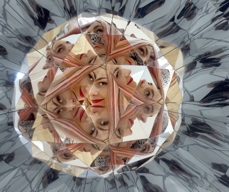 한 여성의 얼굴이 만화경 내부에 여러 번 반사되어 다양한 각도와 표정을 보여줍니다.