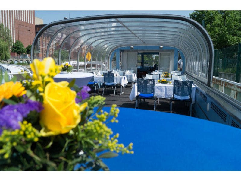 지붕이 투명한 보트에는 노란색 꽃으로 장식된 흰색 천과 파란색 의자가 놓인 테이블이 있습니다.