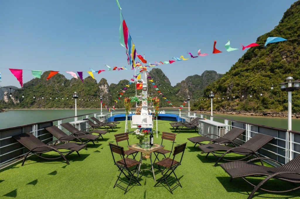 라운지 의자가 있는 보트의 야외 데크, 꽃과 와인이 놓인 테이블, 화려한 깃발. 석회암 절벽을 배경으로.