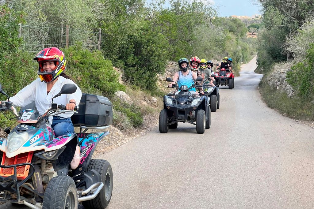 푸르고 숲이 우거진 포장도로에서 쿼드 바이크를 타는 사람들. 전방의 한 사람이 그룹을 이끌고 있습니다.