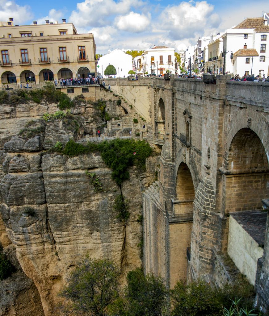 역사적인 석조 다리는 깊은 바위 협곡에 걸쳐 있으며, 두 개의 마을 지역과 건물 및 사람들이 위에서 관찰하는 곳을 연결합니다.