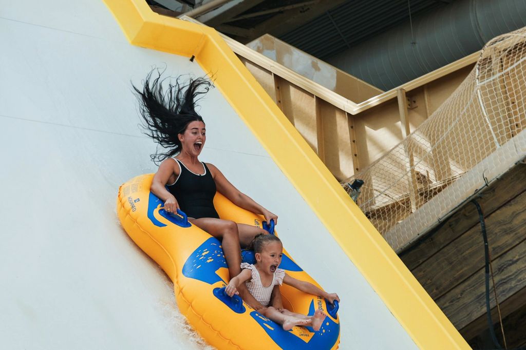 노란색 튜브를 탄 두 사람이 워터 슬라이드를 따라 미끄러지며 신나게 웃고 있습니다.