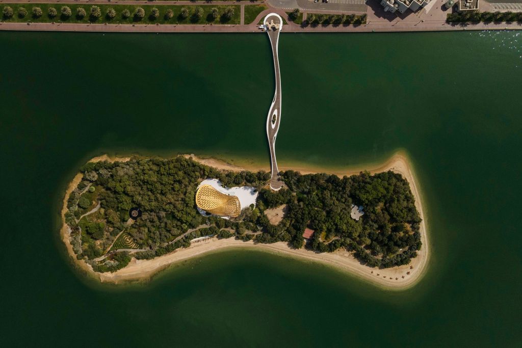 푸른 물 위로 길고 구불구불한 보행자 다리로 본토와 연결된 작고 울창한 섬의 공중 전망.