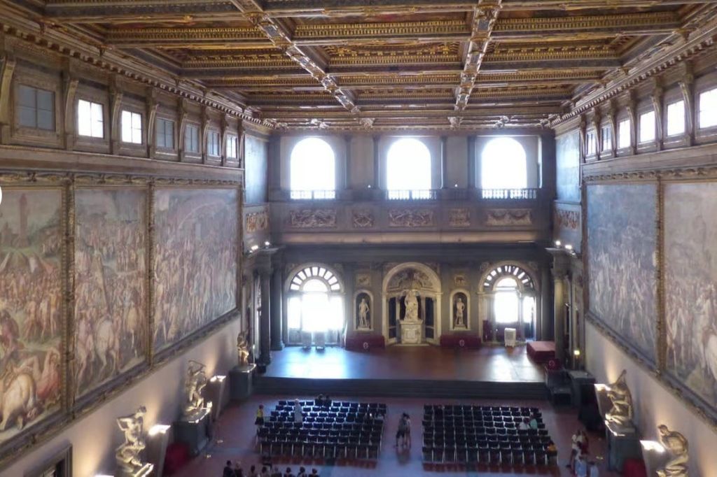 화려한 천장, 커다란 아치형 창문, 조각상, 벽화, 의자, 무대 공간이 있는 그랜드 홀입니다.