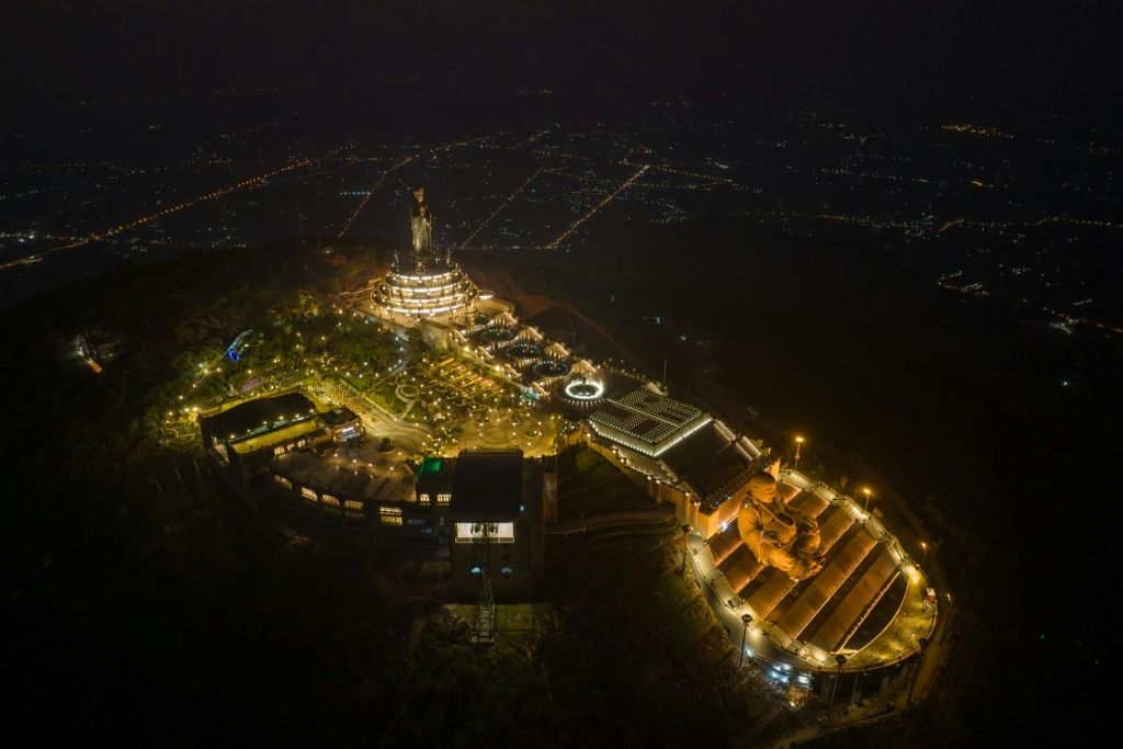 광활한 도시 풍경으로 둘러싸인 높은 동상이 있는 커다란 언덕 꼭대기 사원의 공중 야간 풍경.