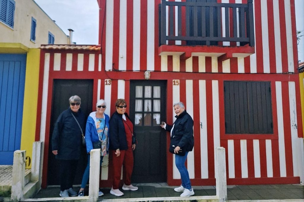 빨간색과 흰색 줄무늬 건물 앞에 서 있는 네 사람이 미소를 짓고 있습니다. 13호와 15호가 보입니다.