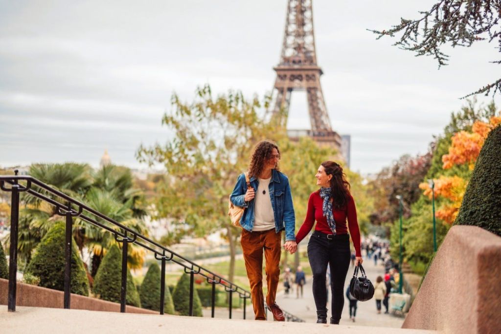 에펠탑 근처 야외에서 나란히 손을 잡고 걷고 있는 한 커플은 흐린 날 나무와 사람들을 배경으로 이야기를 나눕니다.