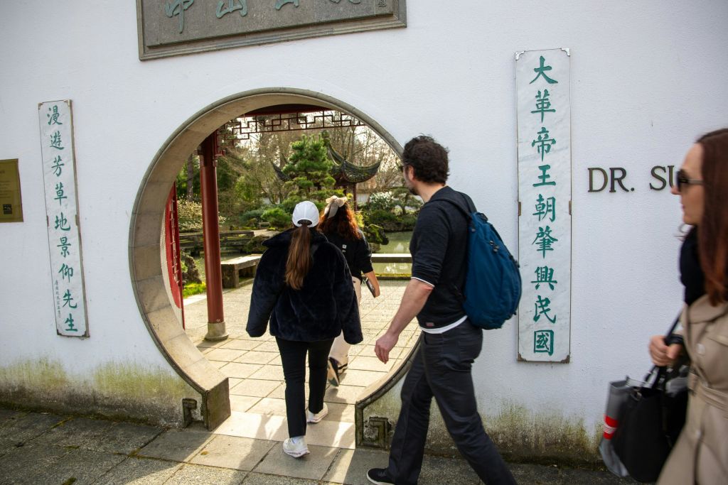 한자가 적힌 하얀 벽의 원형 입구를 지나면 녹음과 전통 건축물이 있는 정원이 나옵니다.