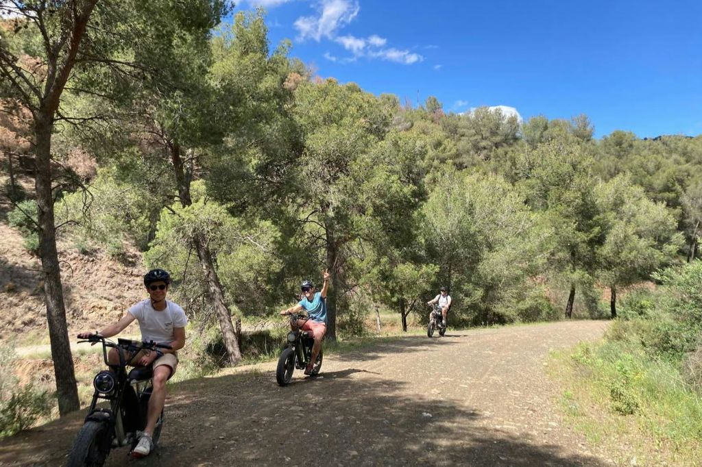 맑고 푸른 하늘 아래 숲이 우거진 흙길에서 오프로드 자전거를 타는 세 사람.