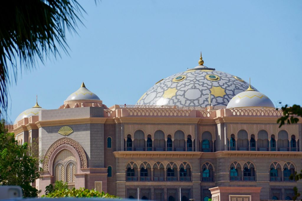 돔, 정교한 디테일, 아치형 창문이 있는 커다란 화려한 건물로, 맑고 푸른 하늘과 야자수 잎을 배경으로 합니다.