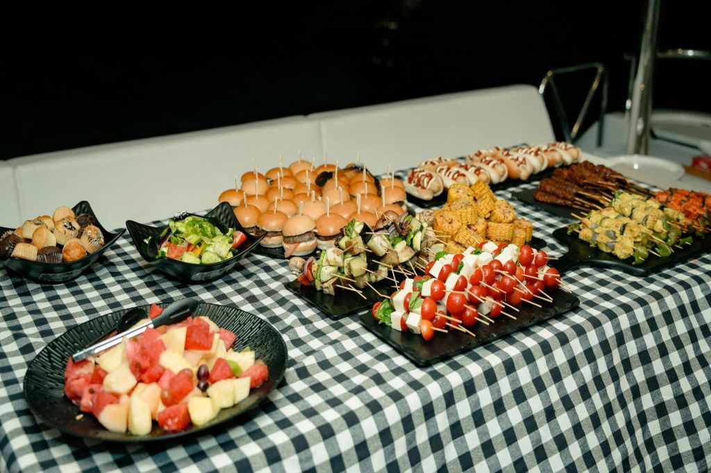 그릇과 트레이에 슬라이더, 꼬치, 옥수수, 과일, 샐러드가 놓인 체크무늬 식탁보입니다.