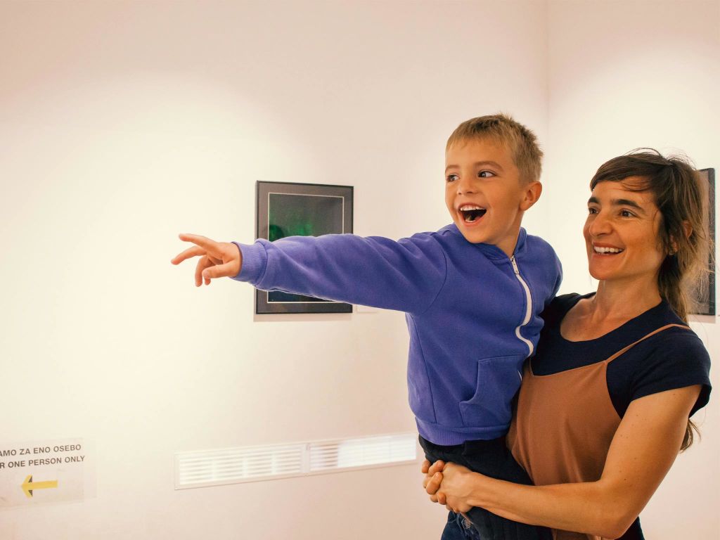 한 여성이 미술관에서 아이를 품에 안고 있습니다. 아이가 신나게 가리키고 있고, 두 아이 모두 미소를 짓고 있습니다.