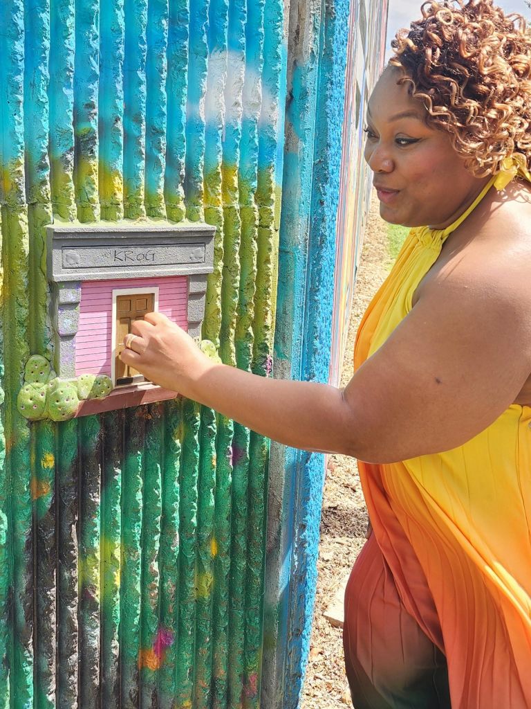 노란색 드레스를 입은 사람이 화려하고 칠해진 야외 표면의 작은 장식 문과 상호 작용합니다.