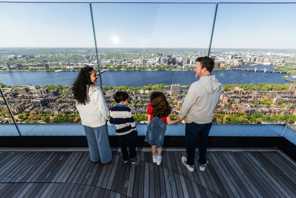 4인 가족이 전망대에 서서 맑은 하늘 아래 도시 풍경과 강을 내려다보고 있습니다.