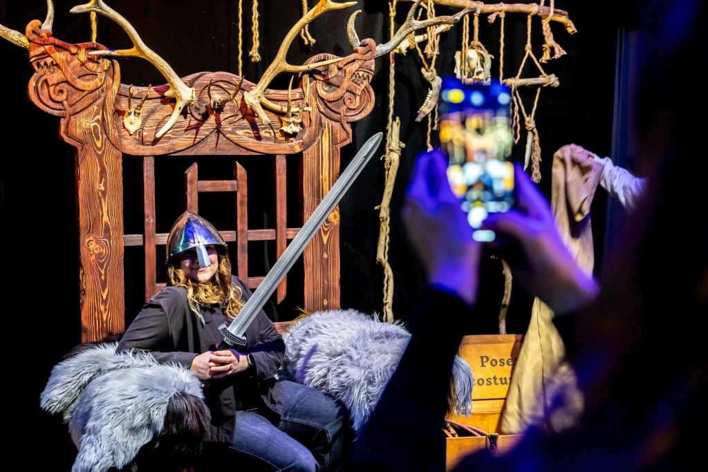 헬멧을 쓰고 칼을 들고 있는 사람이 장식 의자에 앉아 포즈를 취하고, 스마트폰으로 사진을 찍고 있습니다.