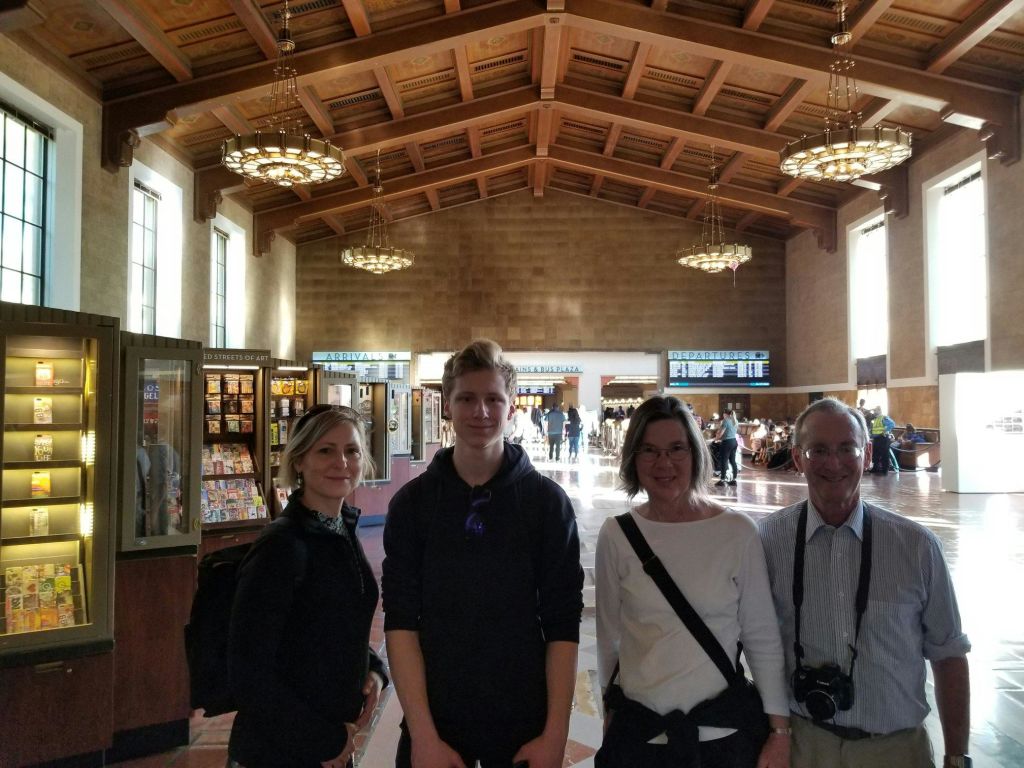 높은 나무 천장과 매달린 샹들리에가 있는 넓은 홀 안에는 4명이 서 있습니다.