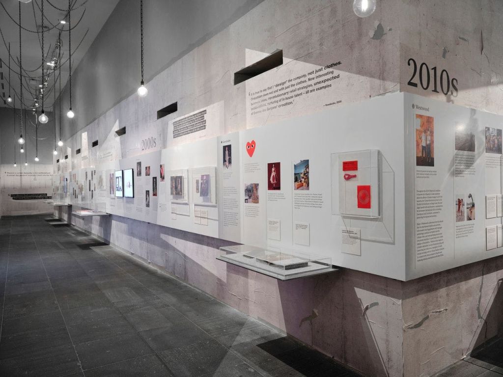 다양한 사물, 이미지 및 텍스트 패널이 벽에 장착된 타임라인을 표시하는 박물관 전시물입니다. 오버헤드 조명이 해당 구역을 비춥니다.