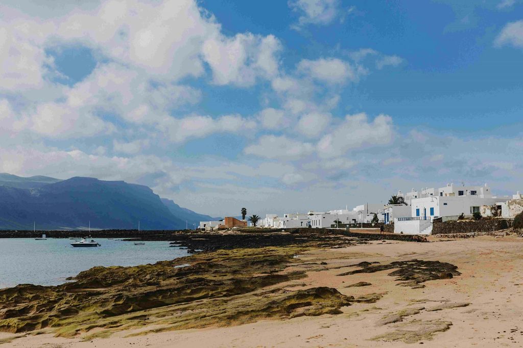 부분적으로 흐린 하늘 아래 하얀 건물과 산맥을 배경으로 한 바위 해안선.