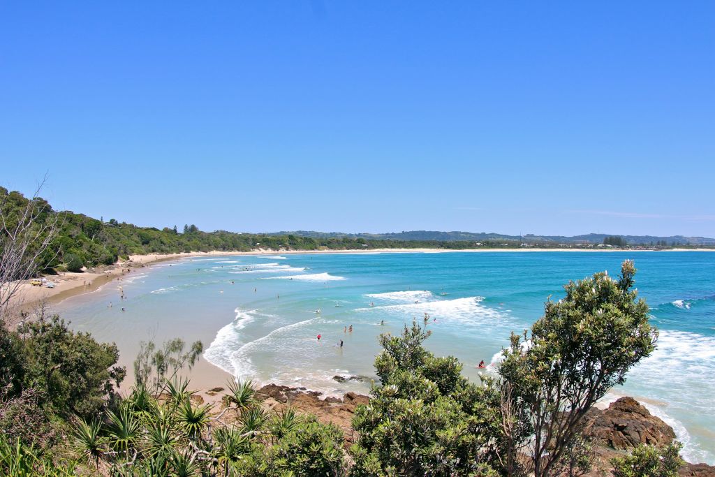 푸르른 녹음과 푸른 하늘로 둘러싸인 청록색의 맑은 물, 파도, 수영하는 사람들로 가득한 깨끗한 해변.