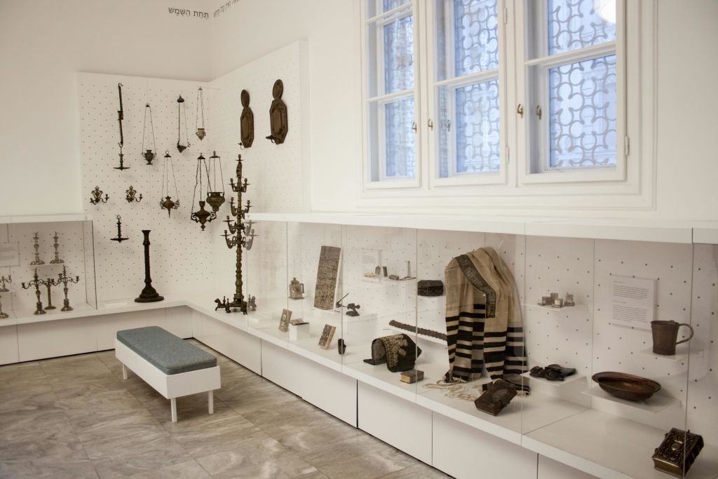 커다란 창문 아래에는 촛대, 기도용 숄, 책 등 종교 유물이 전시된 박물관 전시실이 있습니다.