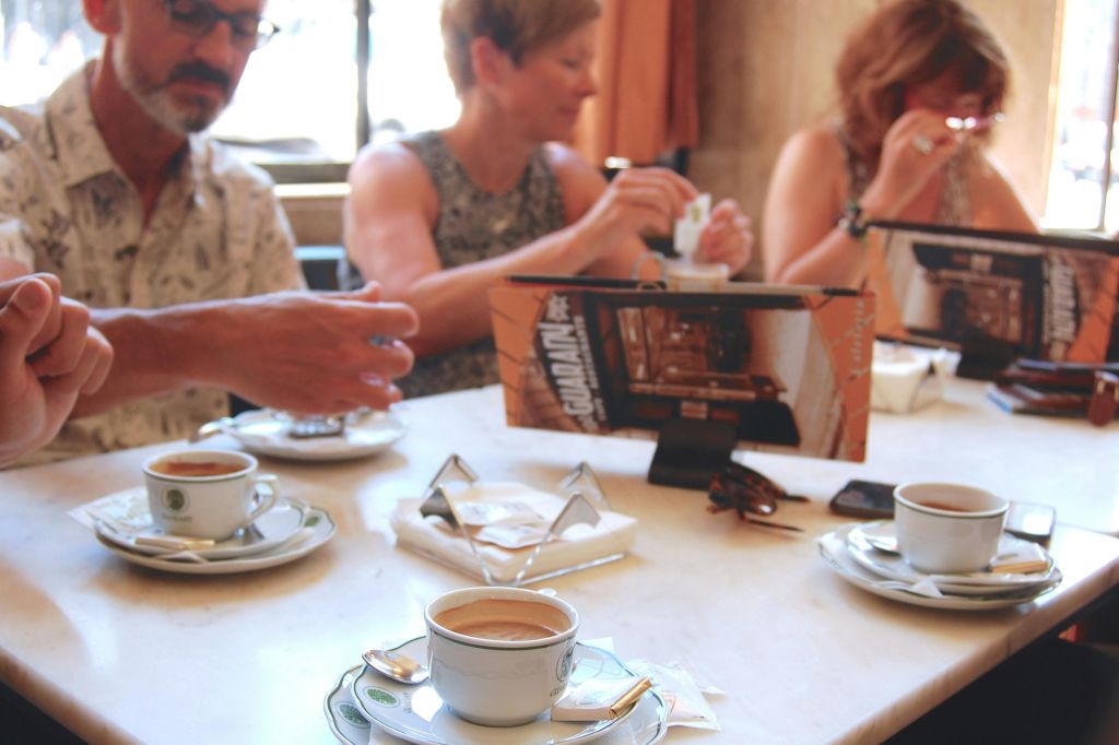 세 사람이 테이블에 앉아 커피를 즐기고 있습니다. 테이블 중앙에 작은 메뉴가 똑바로 놓여 있습니다.