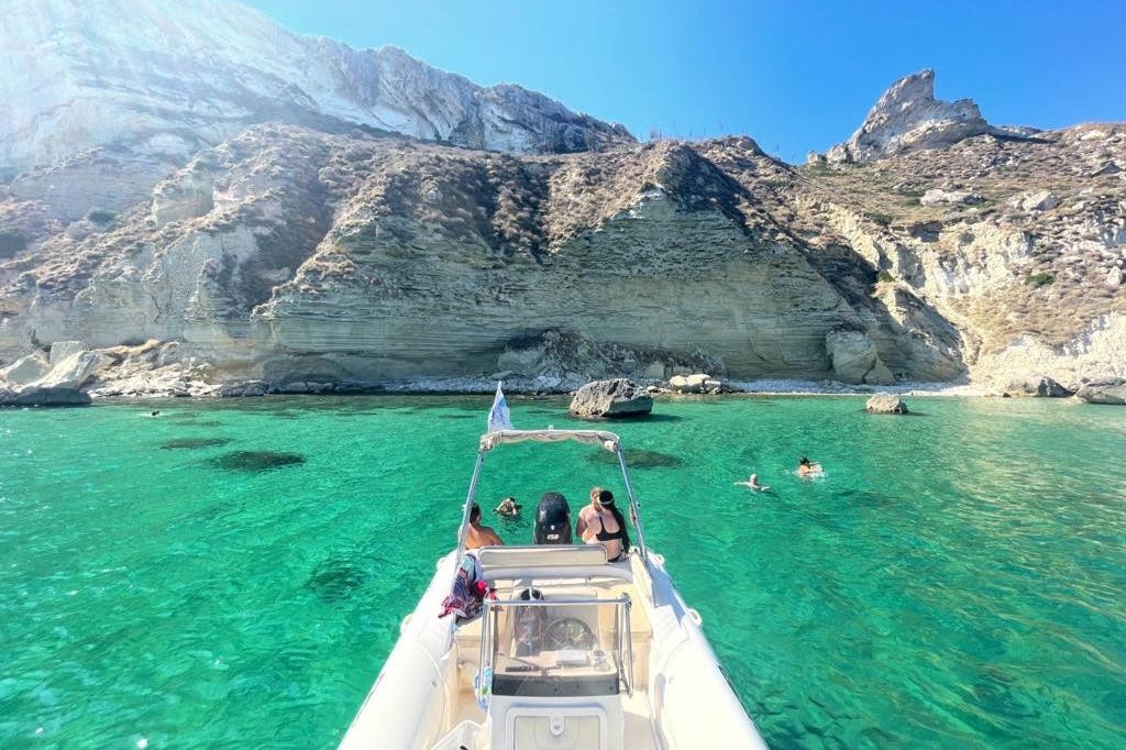 사람들은 화창한 하늘 아래 바위 절벽 근처의 맑고 청록색 바다에서 보트에서 수영과 휴식을 즐깁니다.