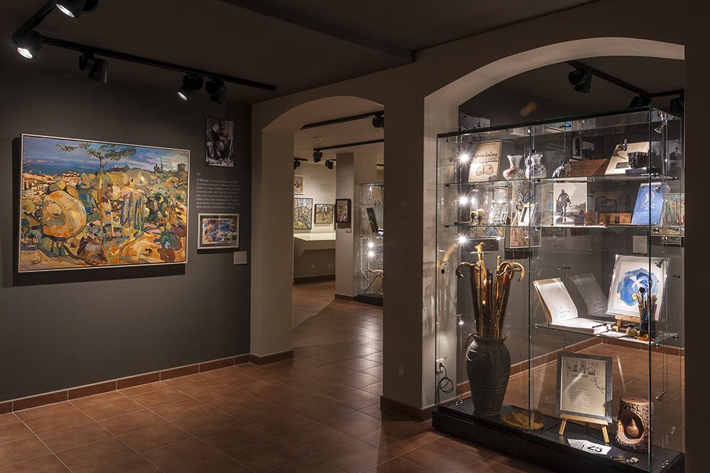 벽에 그려진 그림과 부드러운 조명 아래 유리 케이스에 전시된 유물이 있는 박물관 전시관입니다.