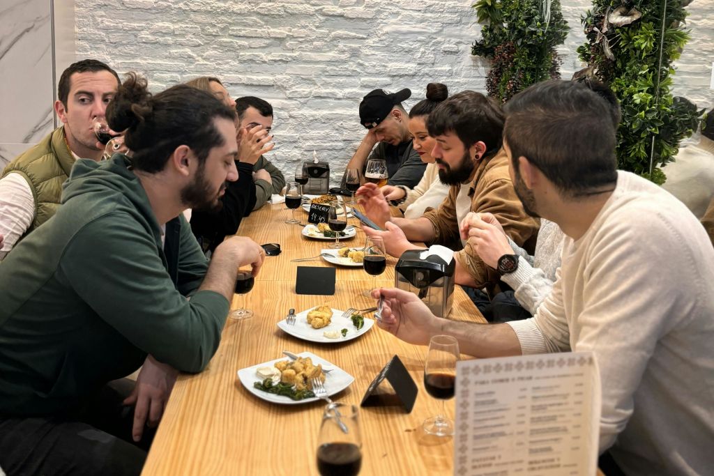 한 무리의 사람들이 나무 테이블에 둘러앉아 하얀 접시의 음식을 먹고 진한 음료를 마시고 있습니다.