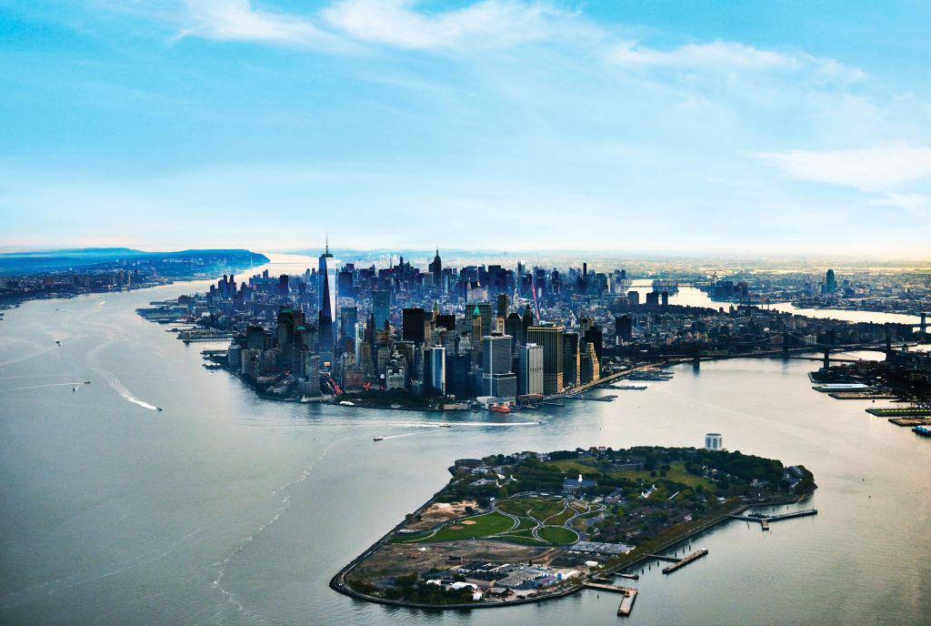 물로 둘러싸인 거대한 고층 건물과 전경에 녹음이 우거진 섬이 있는 맨해튼 스카이라인의 공중 전망.