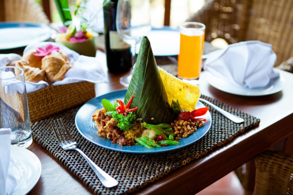 바나나 잎 콘, 야채, 삼발, 크래커, 오렌지 주스를 짠 플레이스매트 위에 올린 인도네시아 음식.