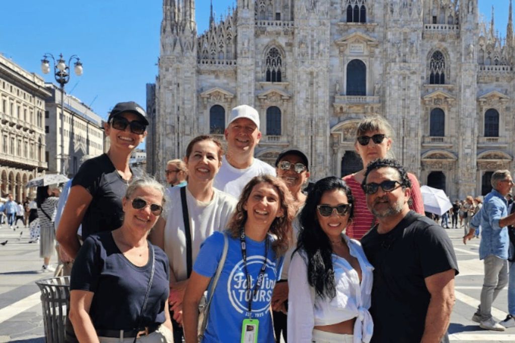 고딕 양식의 건축물과 뾰족한 아치가 있는 크고 화려한 건물 앞에서 웃고 있는 사람들의 일행.