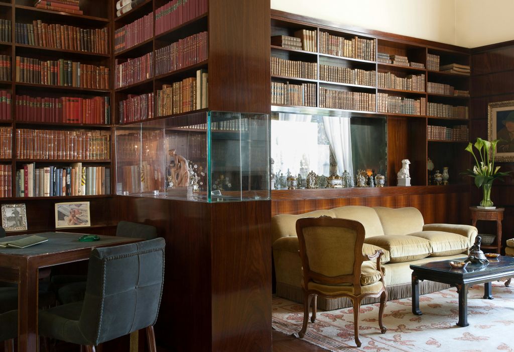 나무 책장, 골동품 책, 유리 진열장, 소파, 안락의자, 의자가 있는 책상이 있는 아늑한 서재입니다.