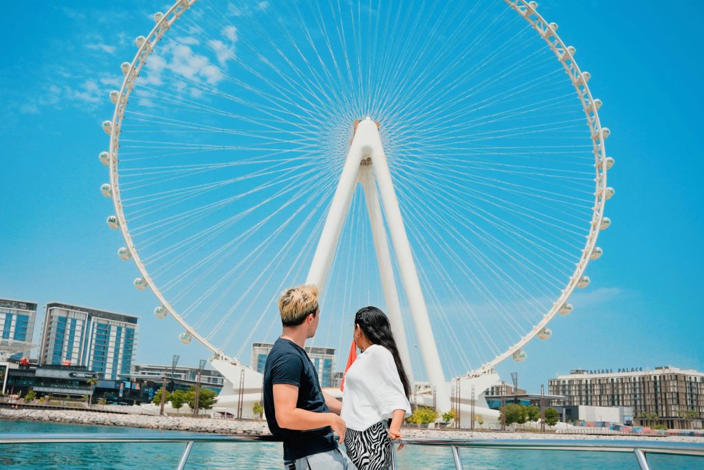 한 남녀가 배에 올라 맑고 푸른 하늘을 배경으로 커다란 대관람차를 바라보고 있습니다.