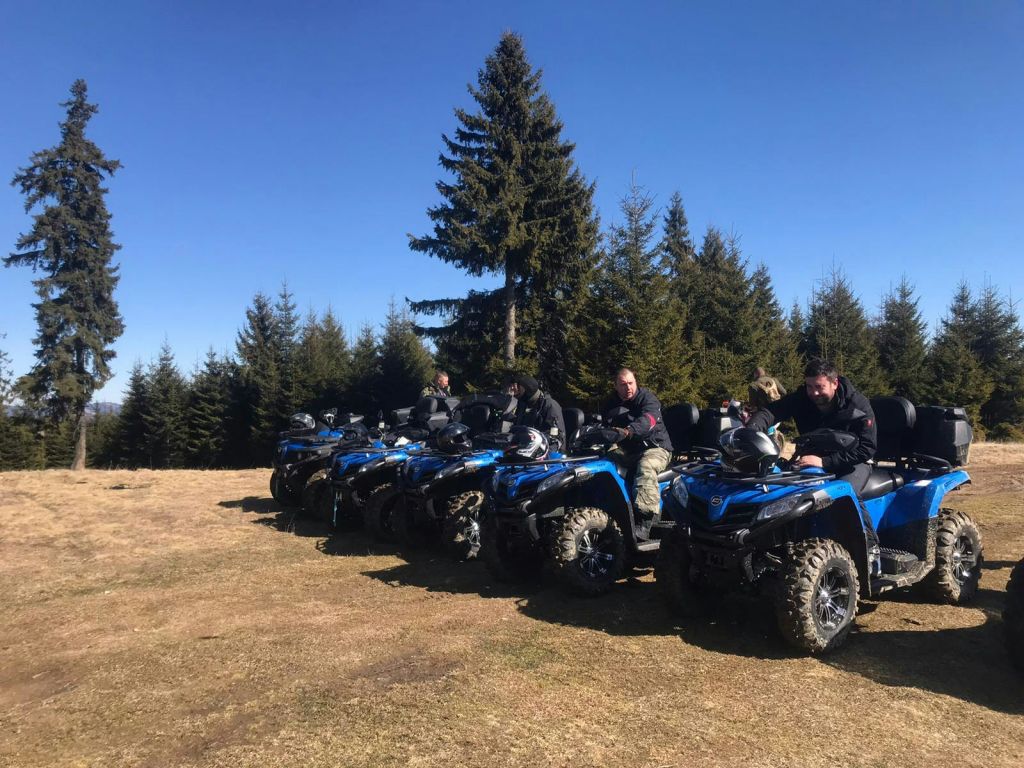 푸른 ATV를 탄 한 무리의 사람들이 높은 상록수를 배경으로 잔디밭에 줄지어 주차하고 있습니다.