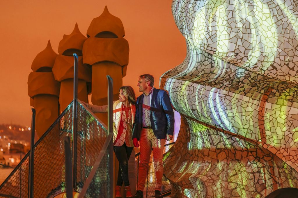 독특하고 화려한 모자이크 구조와 기발하고 둥근 탑을 배경으로 한 남성과 여성이 산책로에 서 있습니다.