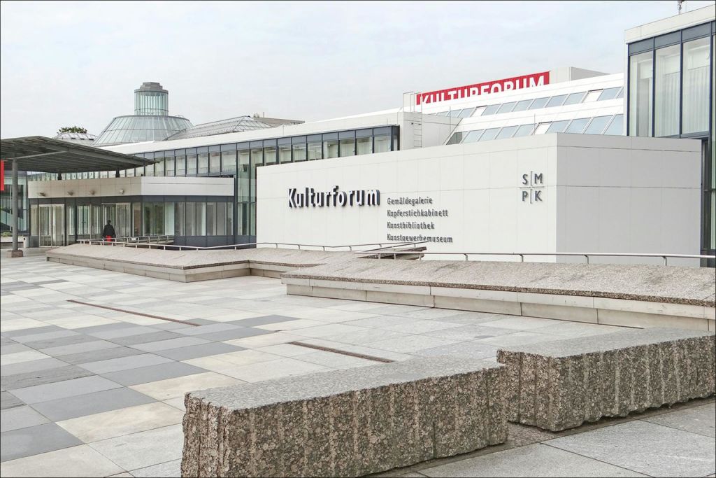 커다란 "Kulturforum" 표지판, 회색 콘크리트 외관, 앞에 광대 한 포장 광장이있는 현대적인 건물 단지.
