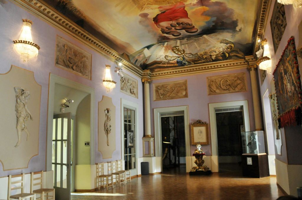 고전 회화, 샹들리에, 장식 천장 예술이 있는 화려한 객실. 여러 개의 의자와 액자에 담긴 예술품이 보입니다.