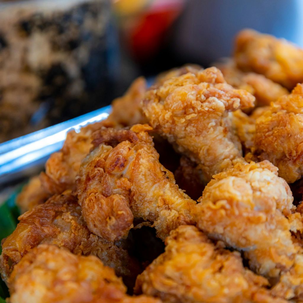 바삭하고 황금빛 갈색 프라이드 치킨 조각이 담긴 트레이의 클로즈업. 흐릿한 배경에는 뚜렷하지 않은 개체가 있습니다.