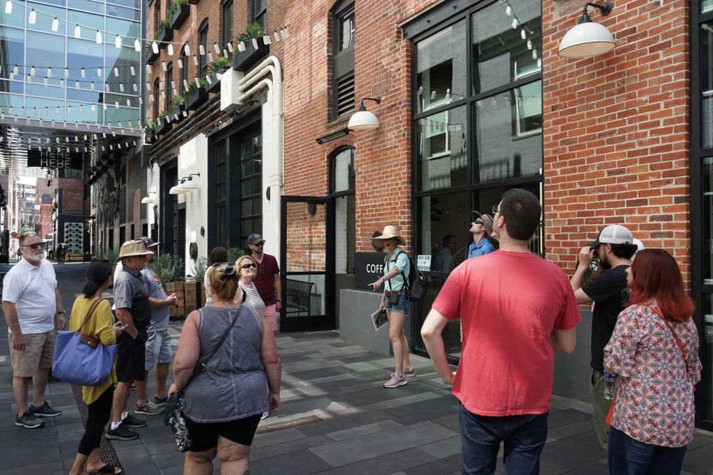 도시 거리의 벽돌 건물 바깥에 서 있는 한 무리의 사람들로 매달린 조명과 도시 인테리어가 돋보입니다.