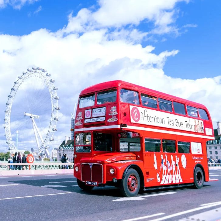 런던 아이 대관람차를 배경으로 도시 거리에 '애프터눈 티 버스 투어' 표지판이 있는 빨간색 2층 버스가 있습니다.