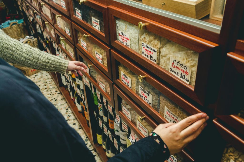 가게에서 다양한 곡물과 병이 구비된 선반이 가득한 라벨이 붙은 서랍을 둘러보는 사람들.