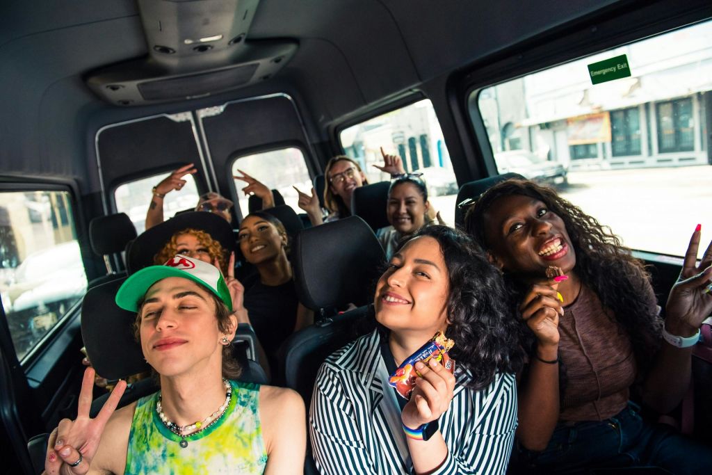 한 무리의 사람들이 밴 안에 앉아 활기차고 편안하게 웃으며 평화 표지판을 만들고 있습니다.